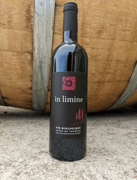 Bouteille de la cuvée In limine, vin rouge du domaine Les Robes Noires, devant une barrique de chêne.
