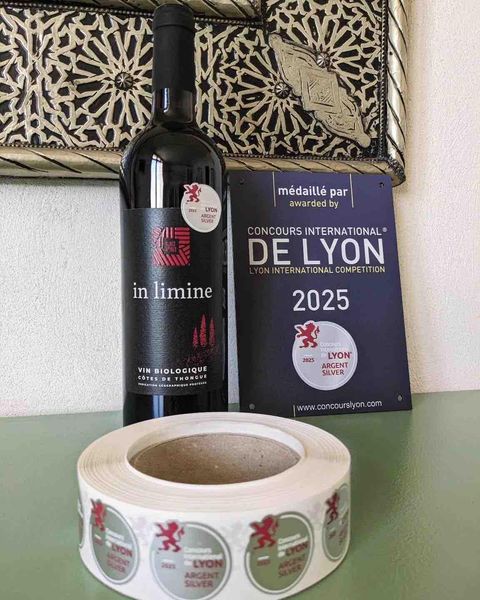 Bouteille d’In limine devant la plaque du Concours International de Lyon 2025 et un rouleau de macarons « argent ».