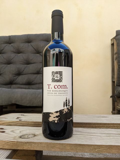 Bouteille de la cuvée T. com., vin rouge du domaine Les Robes Noires, posée sur une table en bois.